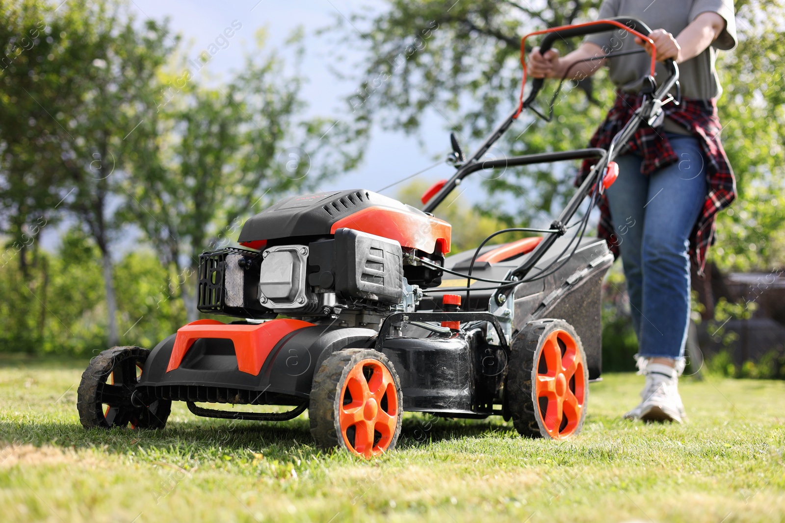 Photo of Woman cutting green grass with lawn mower in garden, selective focus