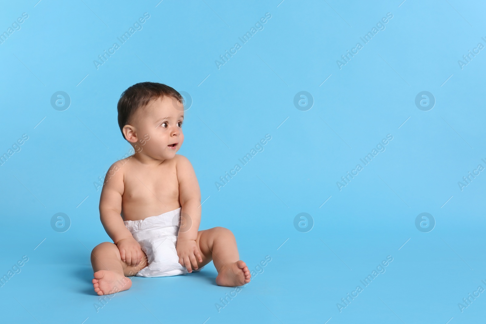 Photo of Cute baby in dry soft diaper sitting on light blue background. Space for text