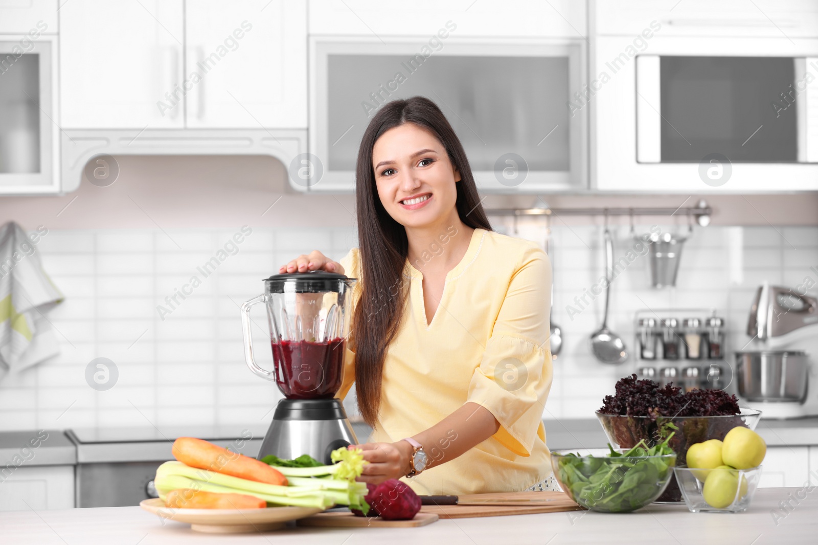 Photo of Young woman preparing tasty healthy smoothie at table in kitchen