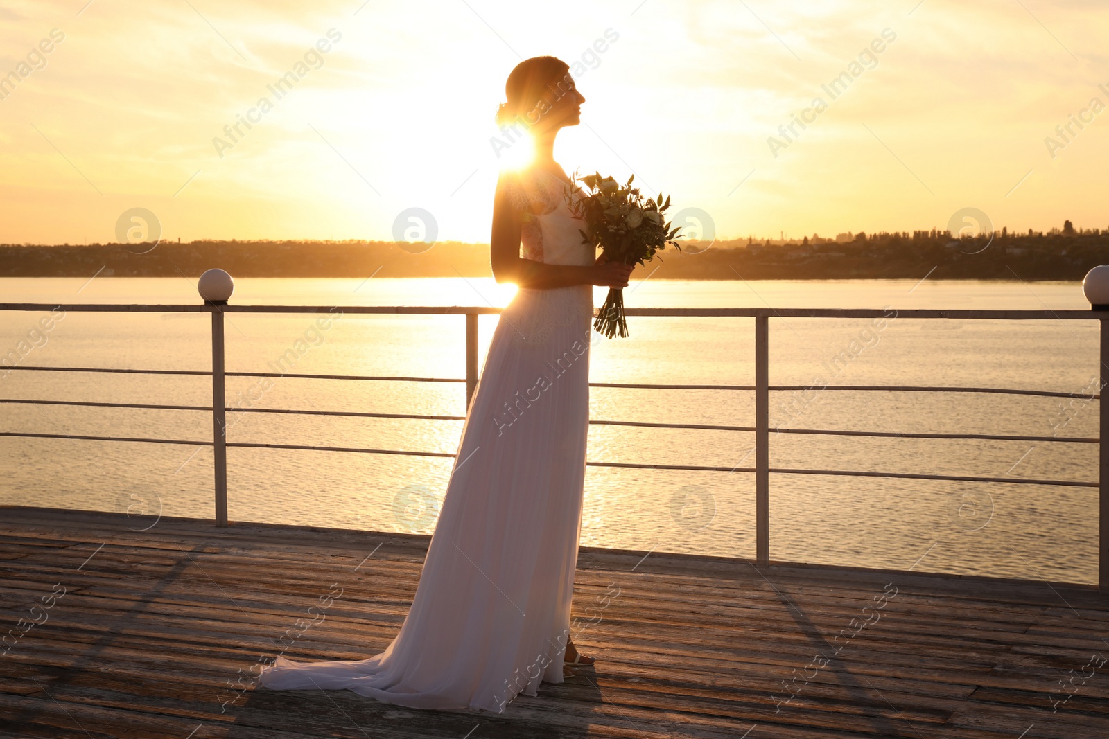 Photo of Gorgeous bride in beautiful wedding dress with bouquet near river on sunset