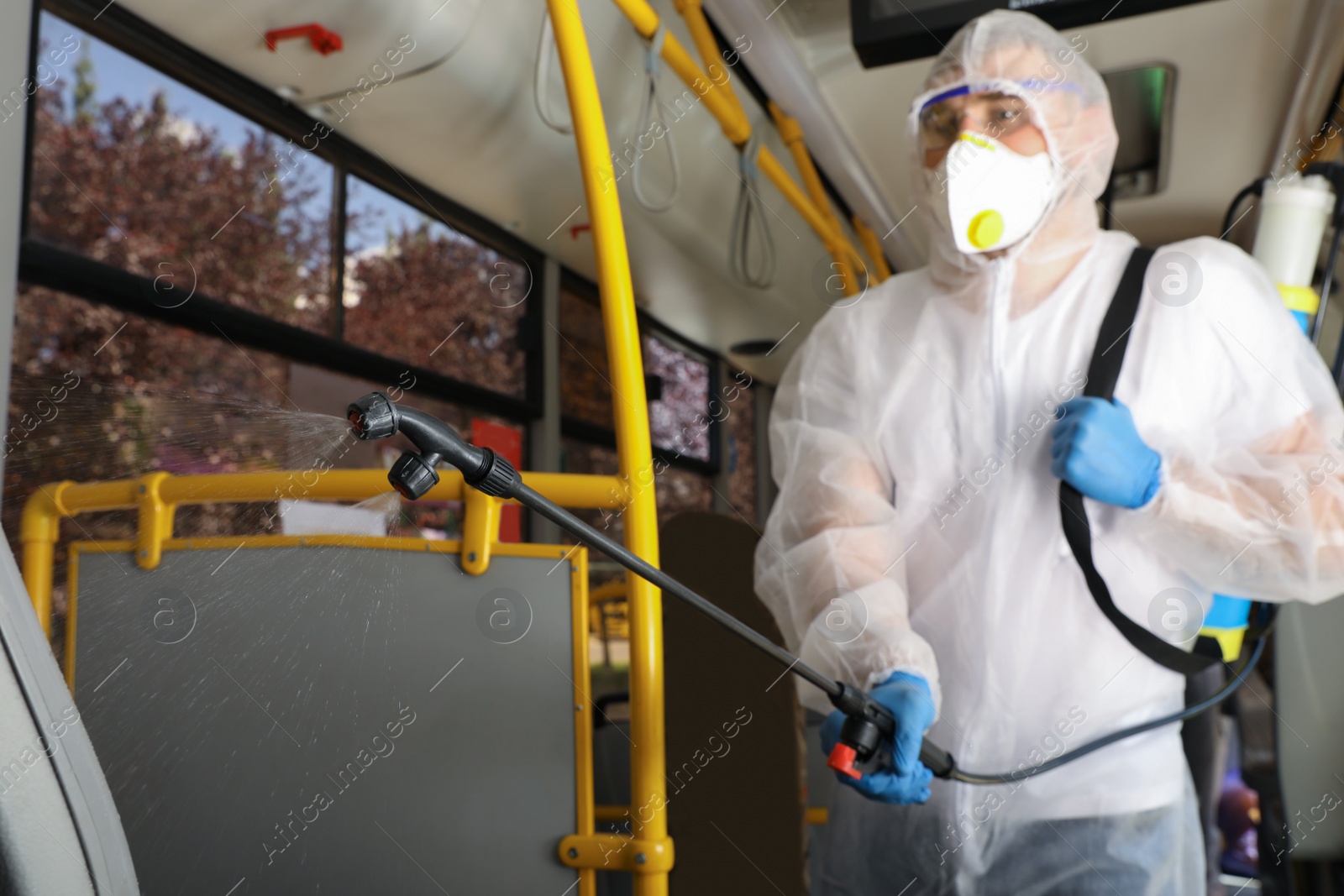 Photo of Public transport sanitation. Worker in protective suit disinfecting bus salon, focus on spray machine nozzle