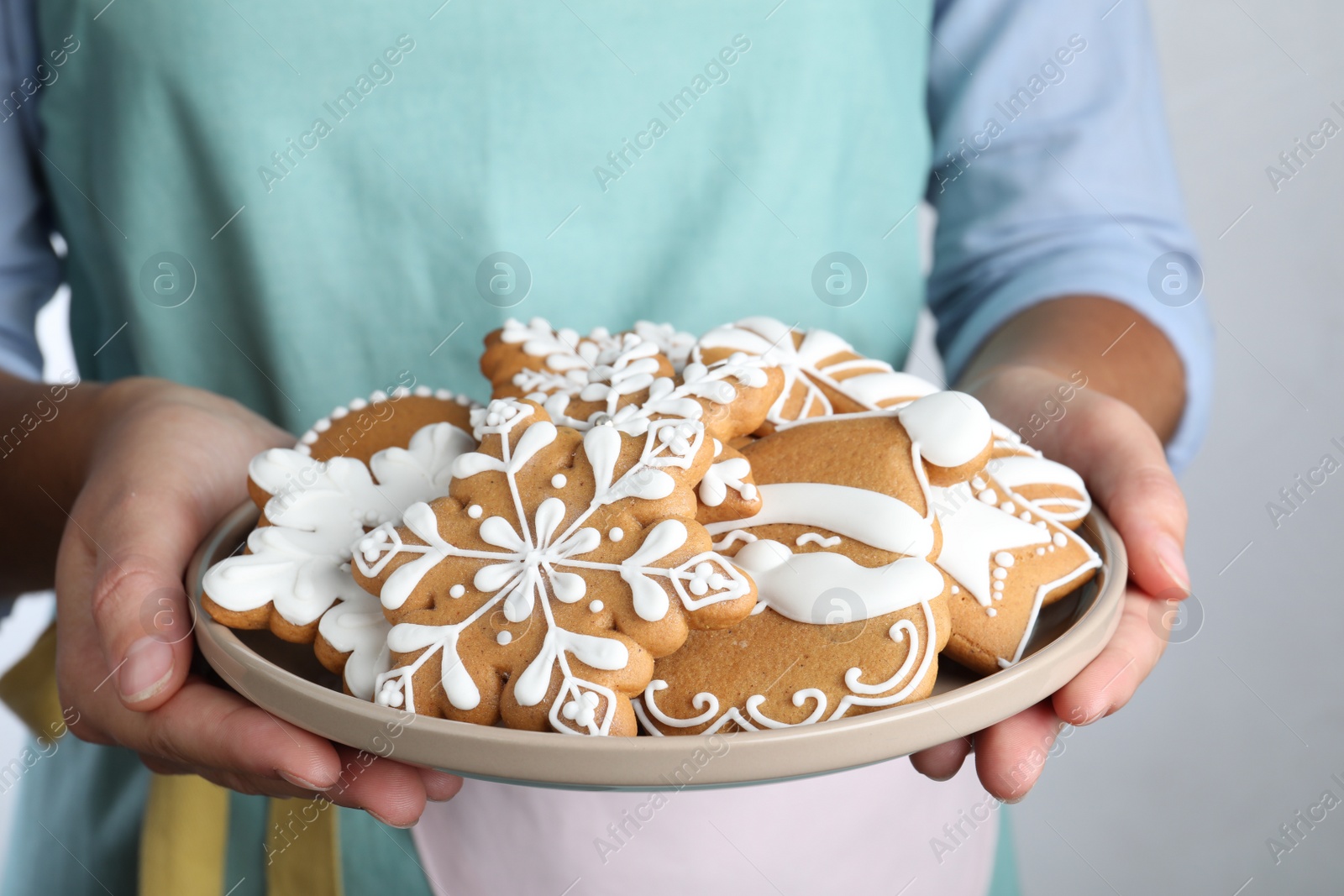 Photo of Woman with plate of delicious gingerbread Christmas cookies on grey background, closeup