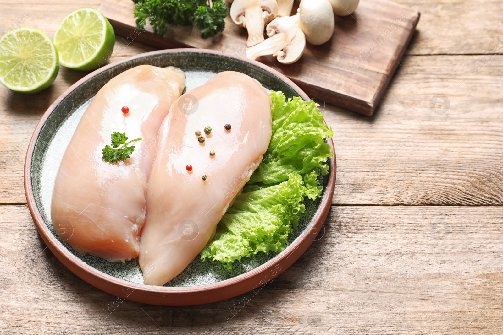 Photo of Plate with raw chicken breasts and ingredients on wooden table. Space for text