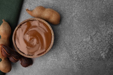 Photo of Bowl of tamarind sauce and fresh pods on brown table, flat lay. Space for text