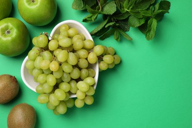 Photo of Fresh ripe grape, kiwis, apples and mint on green background, flat lay. Space for text