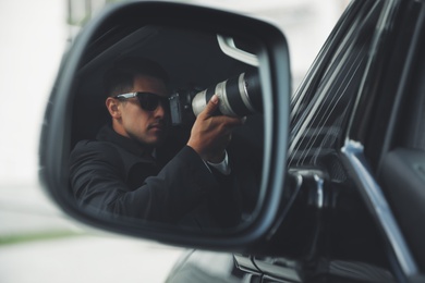 Private detective with camera spying from auto, view through car side mirror