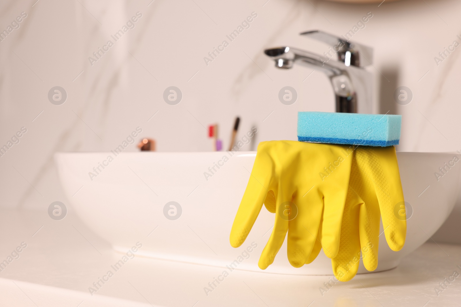 Photo of Sponge and rubber gloves on bathroom sink indoors. Space for text