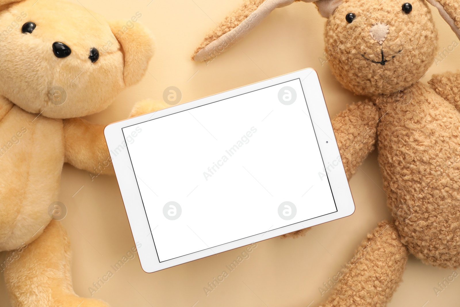 Photo of Modern tablet and stuffed animals on beige background, flat lay. Space for text