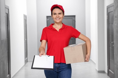 Photo of Smiling courier holding parcel and clipboard indoors