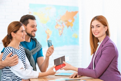 Photo of Female manager giving passports with tickets to couple in travel agency