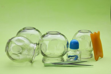 Photo of Glass cups and other equipment for cupping therapy on light green background