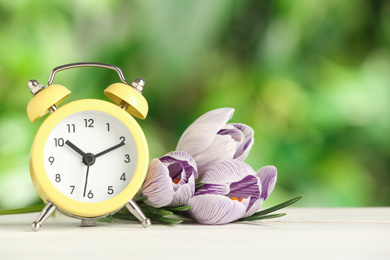Alarm clock and beautiful spring flowers on white wooden table. Time change concept