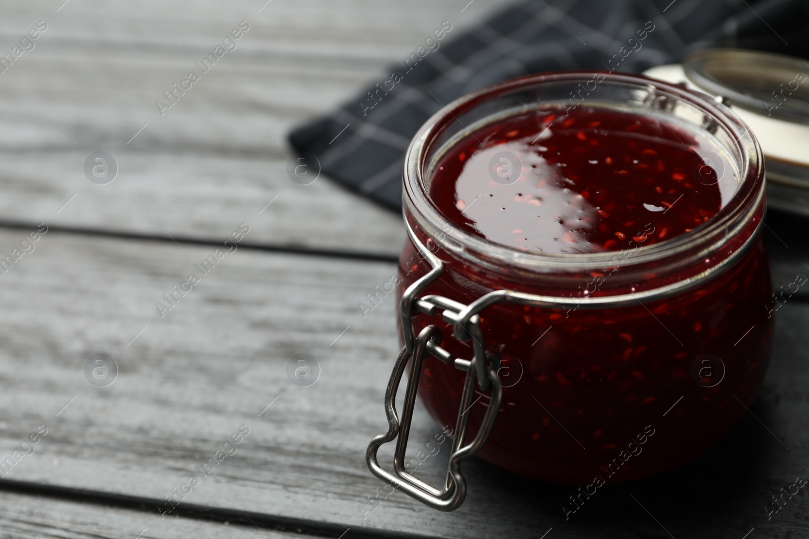 Photo of Homemade delicious raspberry jam on grey wooden table. Space for text