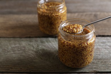 Photo of Jars and spoon of whole grain mustard on wooden table, closeup. Space for text