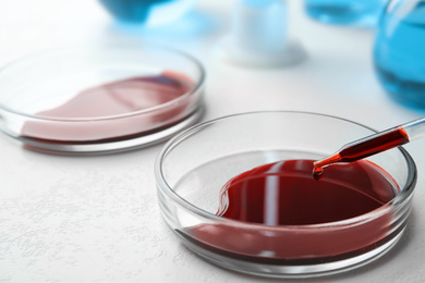 Image of Dripping blood from pipette into Petri dish on table, closeup. Laboratory analysis