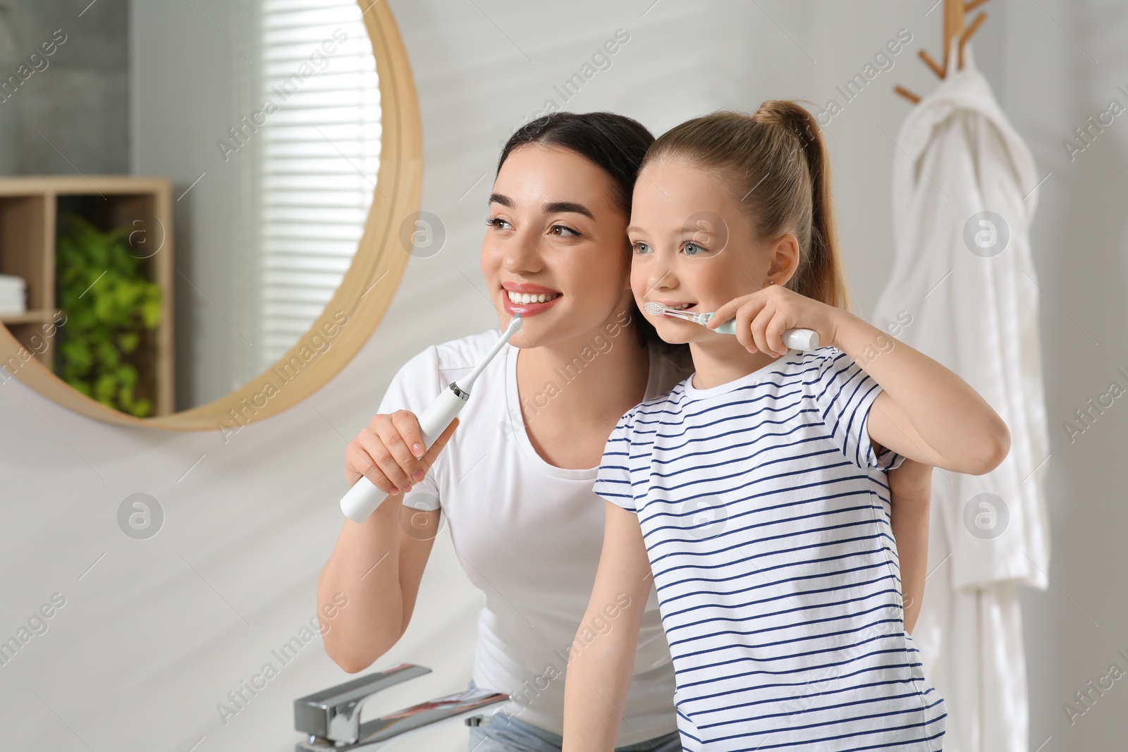 Photo of Mother and her daughter brushing teeth together in bathroom