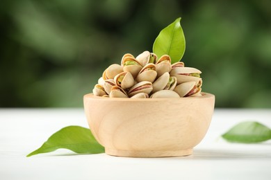 Photo of Tasty pistachios in bowl on white wooden table against blurred background, closeup