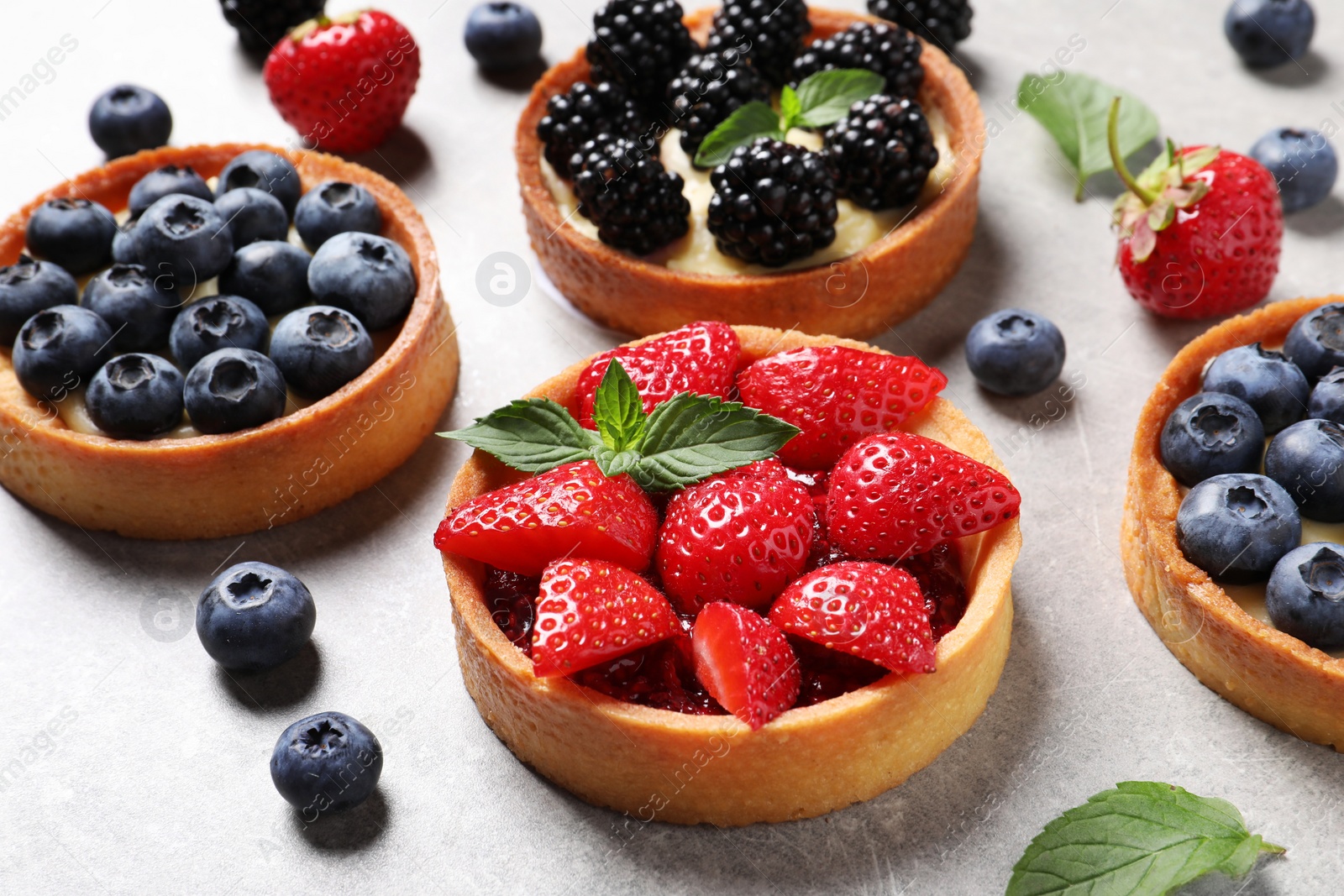 Photo of Tartlets with different fresh berries on light grey table. Delicious dessert