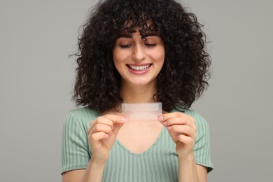 Photo of Young woman holding teeth whitening strips on grey background