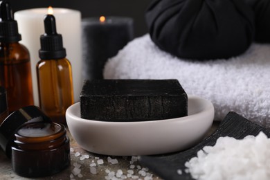 Photo of Spa composition. Black soap bar, sea salt, jar of cream and towels on table, closeup