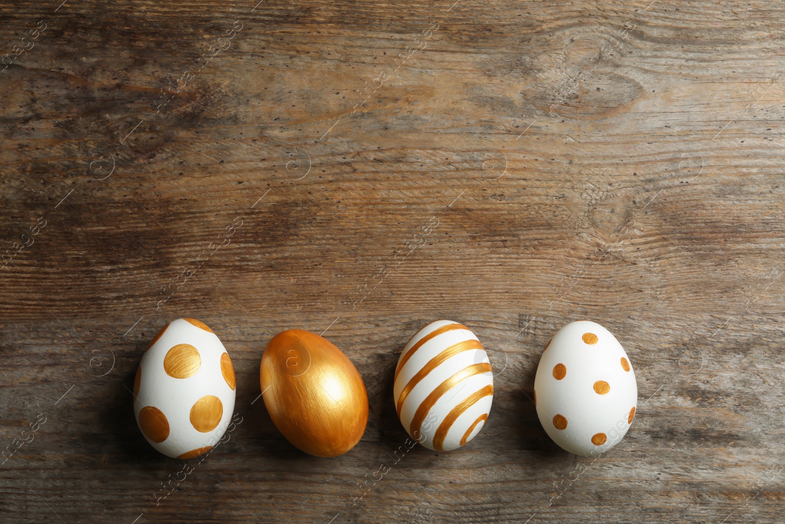 Photo of Set of traditional Easter eggs decorated with golden paint on wooden background, top view. Space for text