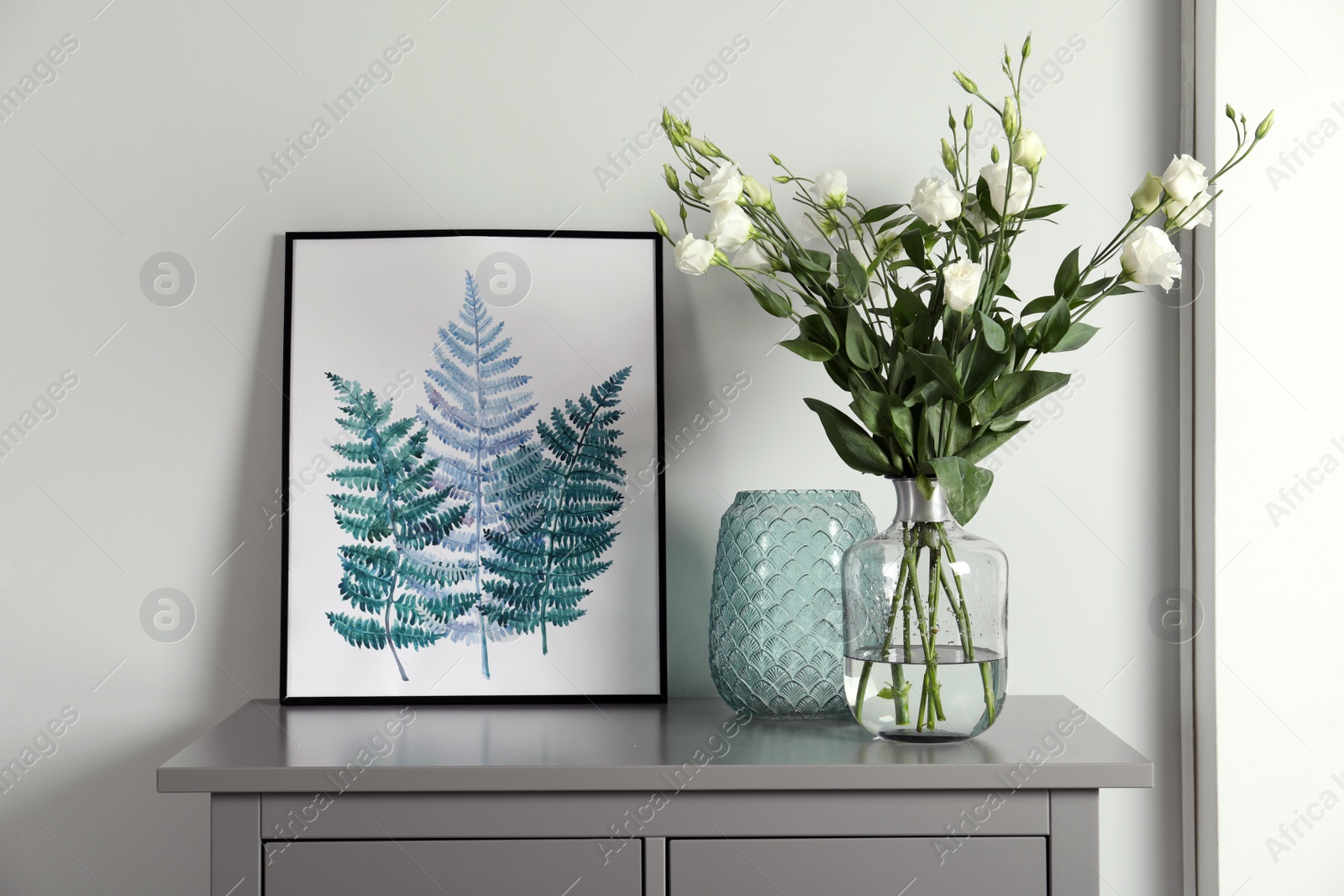 Photo of Composition with eustoma flowers in glass vase on grey cabinet indoors