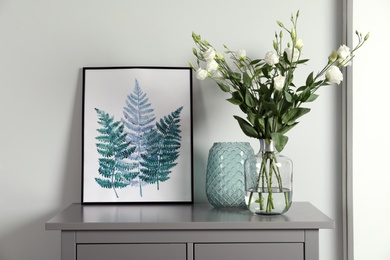 Photo of Composition with eustoma flowers in glass vase on grey cabinet indoors