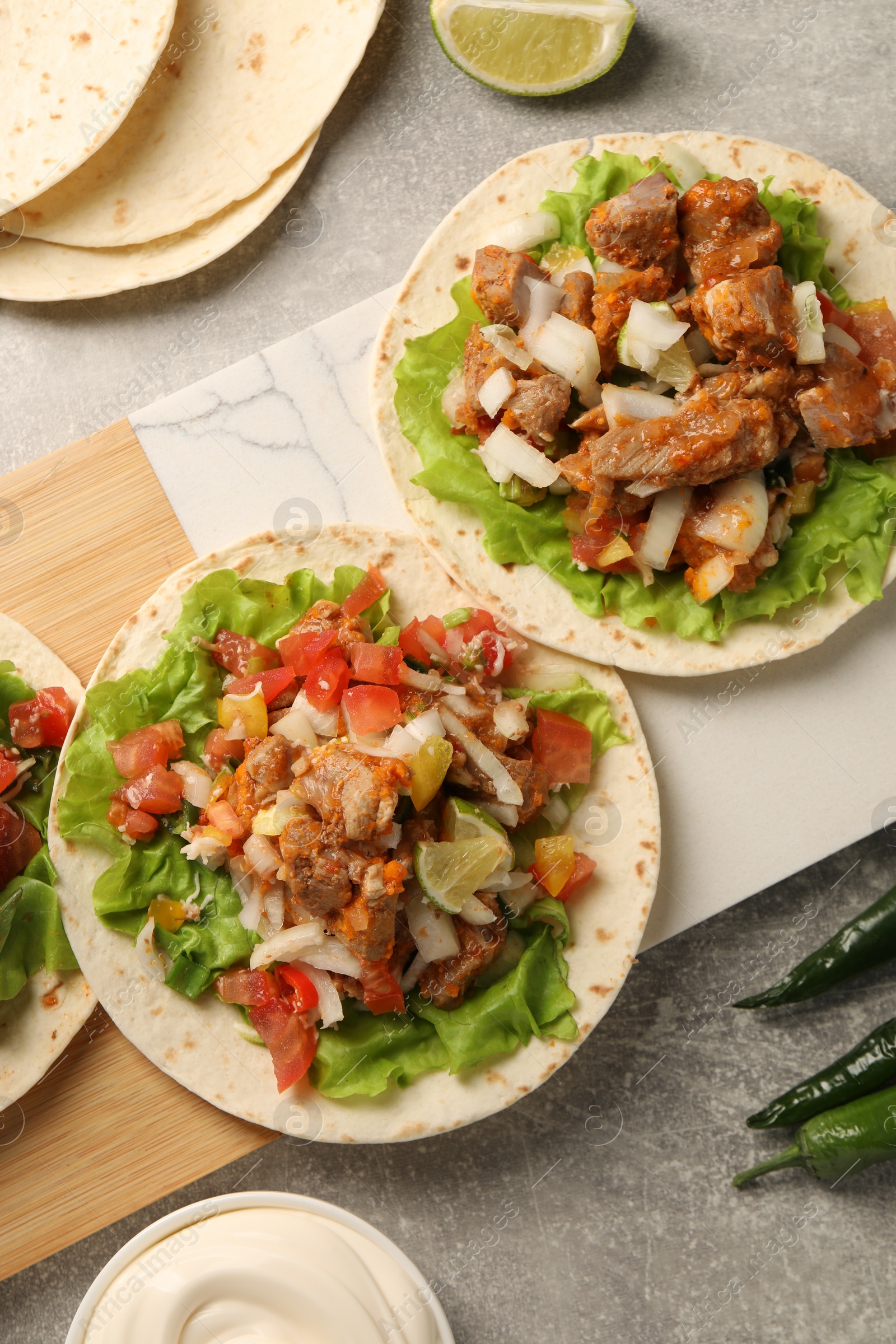 Photo of Delicious tacos with vegetables and meat on grey textured table, flat lay