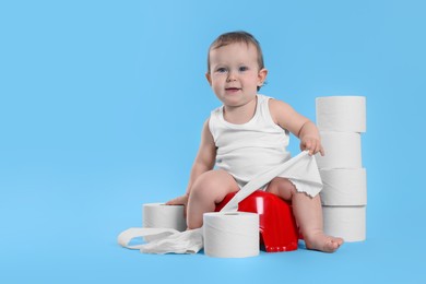 Little child sitting on baby potty and stack of toilet paper rolls against light blue background. Space for text