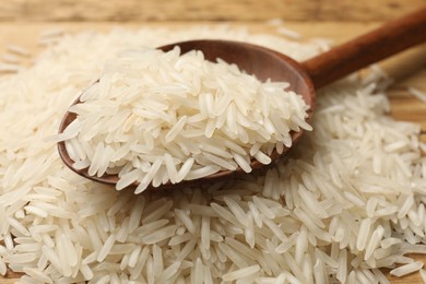 Photo of Raw basmati rice with wooden spoon on table, closeup