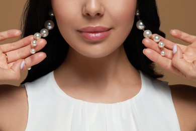 Young woman wearing elegant pearl earrings on brown background, closeup