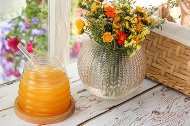 Photo of Delicious fresh honey and beautiful flowers on white wooden table indoors
