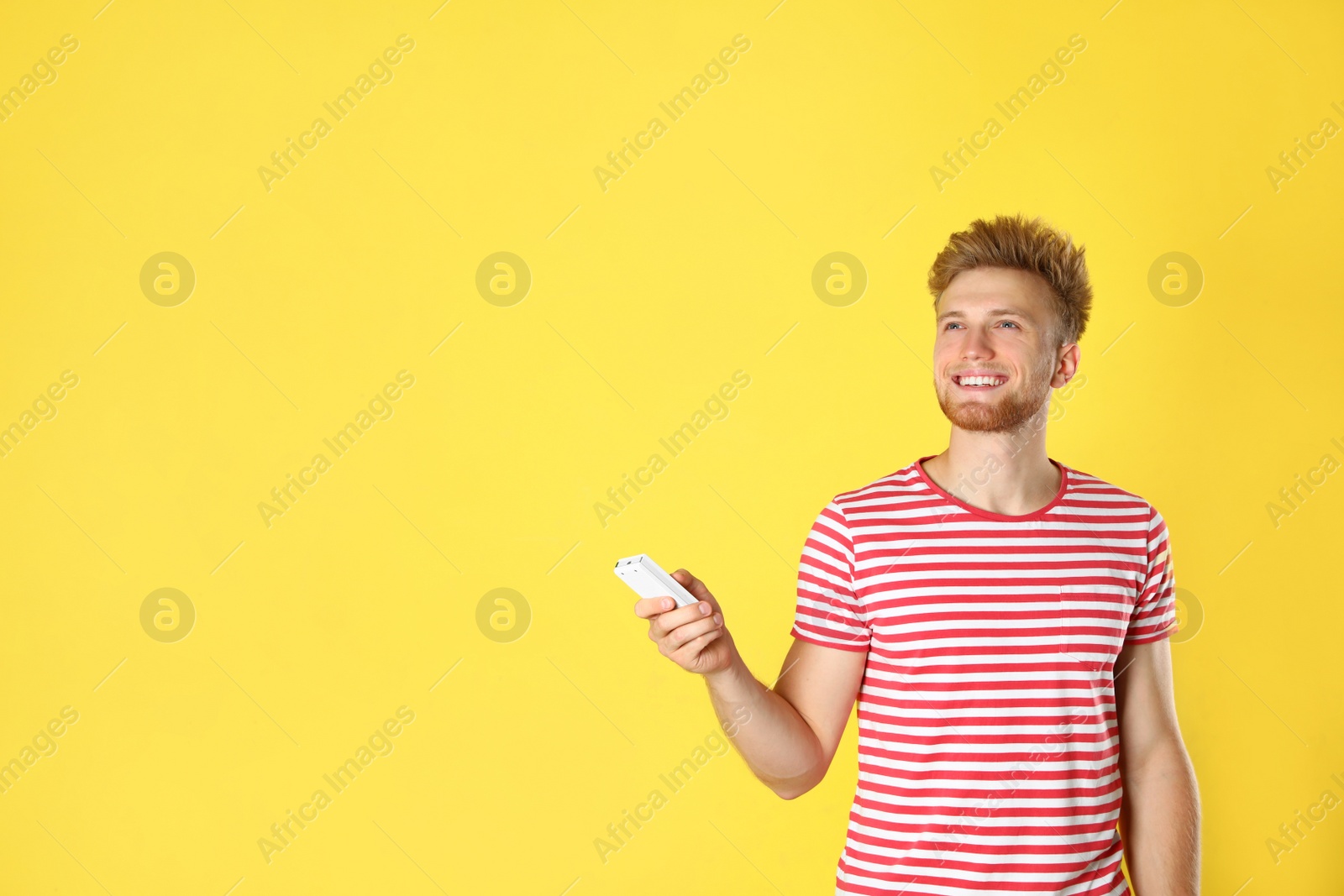 Photo of Young man with air conditioner remote on yellow background. Space for text