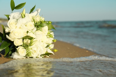 Photo of Beautiful wedding bouquet on sandy beach near sea. Space for text