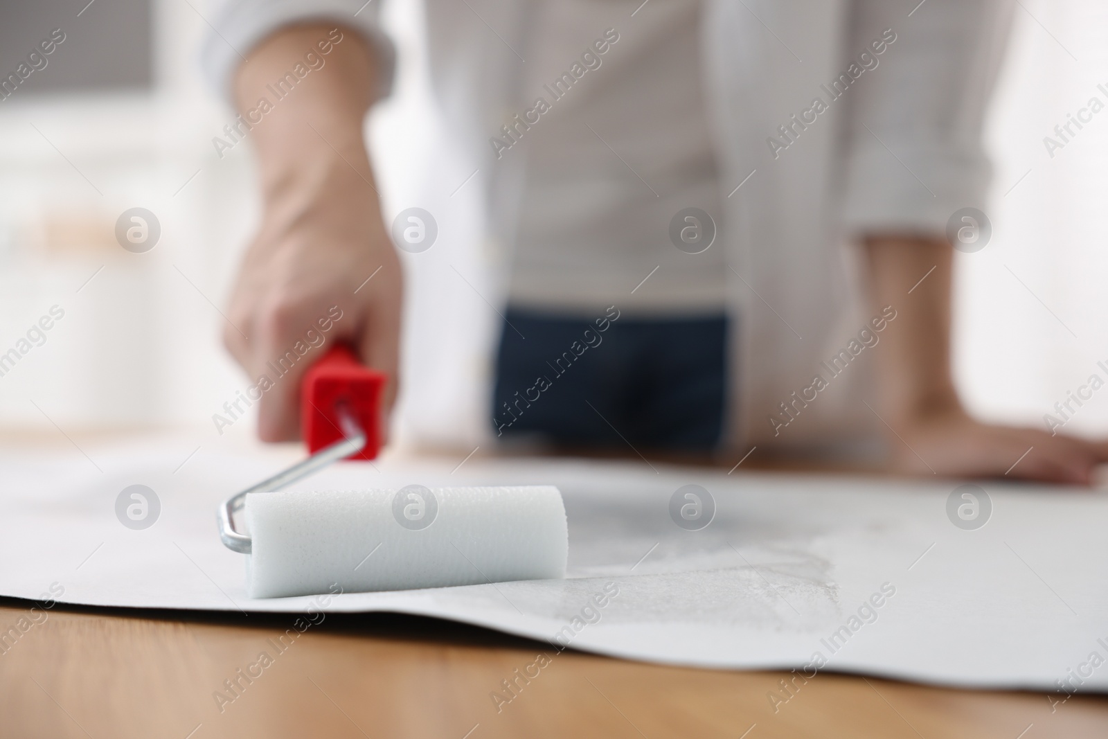 Photo of Man applying glue onto wallpaper sheet at table indoors, closeup