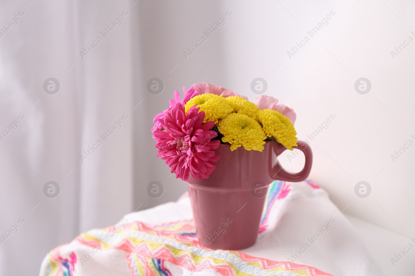 Photo of Beautiful bright flowers in pink cup and fabric on table indoors