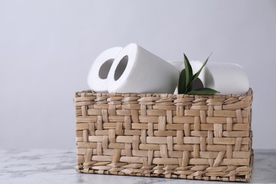 Photo of Toilet paper rolls and green leaves in wicker basket on white marble table