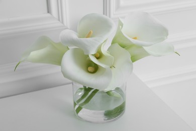 Photo of Beautiful calla lily flowers in glass vase on white table, closeup