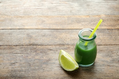 Photo of Glass bottle of wheat grass juice with citrus fruit on wooden background. Space for text