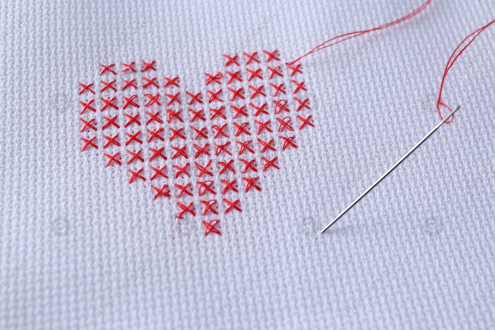 Photo of Embroidered red heart and needle on white cloth, closeup