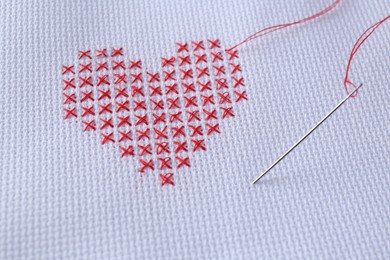 Photo of Embroidered red heart and needle on white cloth, closeup