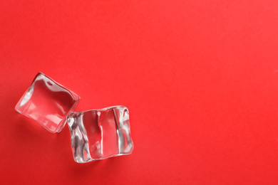 Photo of Crystal clear ice cubes on red background, flat lay. Space for text