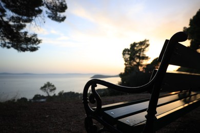 Photo of Wooden bench near seaside at sunset, selective focus. Space for text