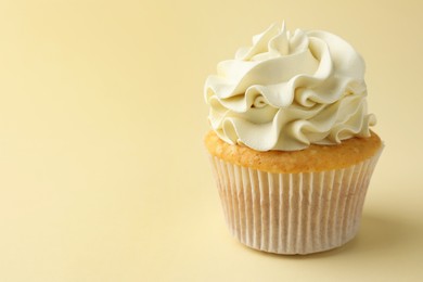 Photo of Tasty vanilla cupcake with cream on pale yellow background, closeup. Space for text