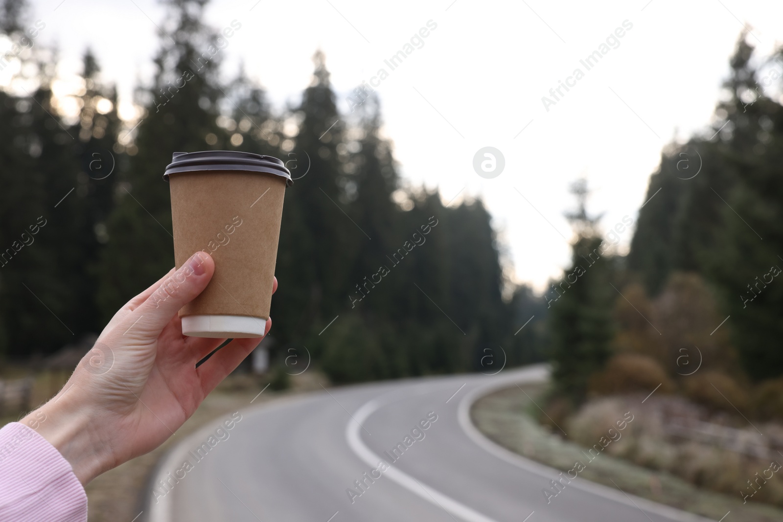 Photo of Woman holding takeaway cardboard coffee cup near road outdoors, closeup. Autumn season