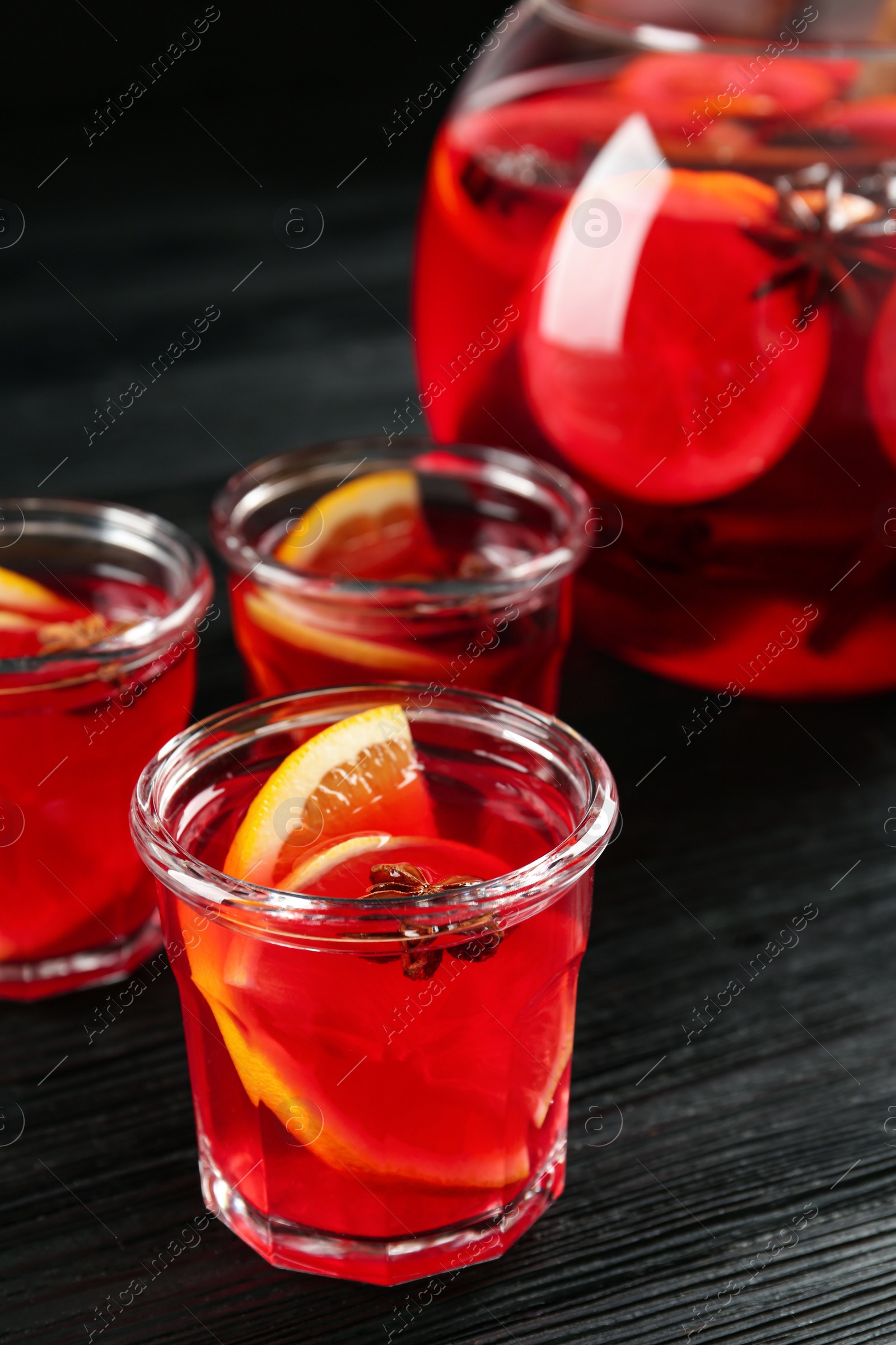 Photo of Bowl and glasses of delicious aromatic punch drink on black wooden table