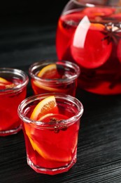 Photo of Bowl and glasses of delicious aromatic punch drink on black wooden table