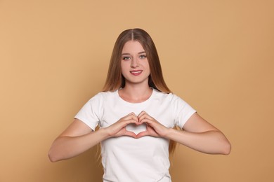 Young woman making heart with hands on beige background. Volunteer concept