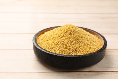 Millet groats in bowl on light wooden table, space for text