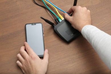 Photo of Man with smartphone connecting to internet via Wi-Fi router at wooden table, closeup